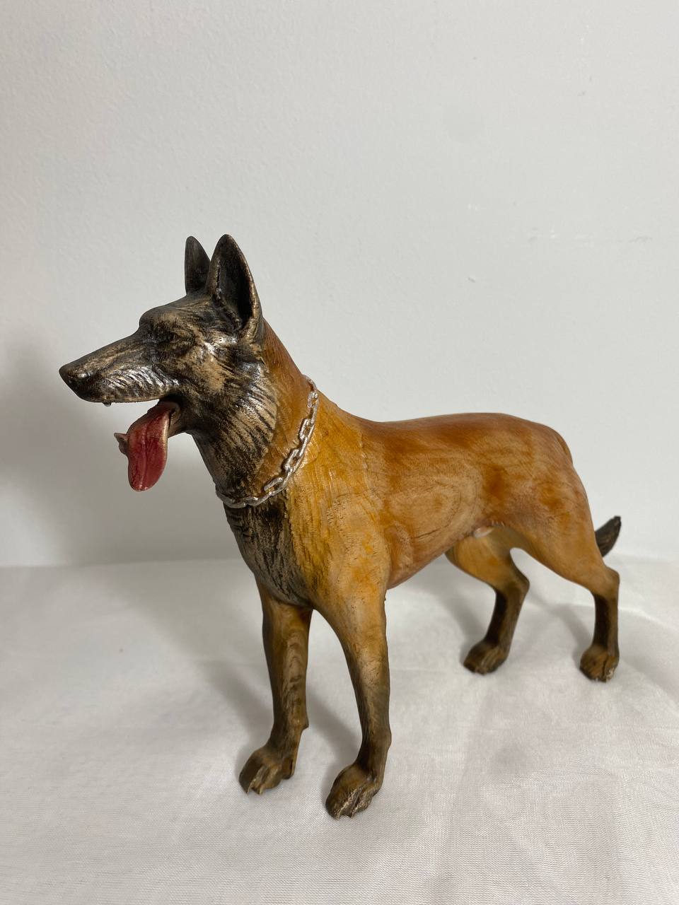 A wooden statue of a Belgian Malinois dog, with a lacquer coating, standing on a plain background.