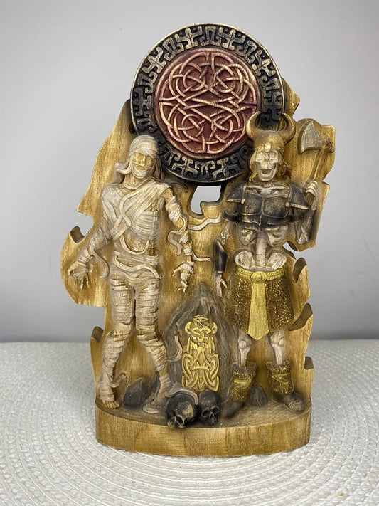 Hand-carved wooden statue depicting an Egyptian mummy and Norse warrior figure with symbolic carvings, skull details, and Celtic knot ornament, inspired by ancient mythology.