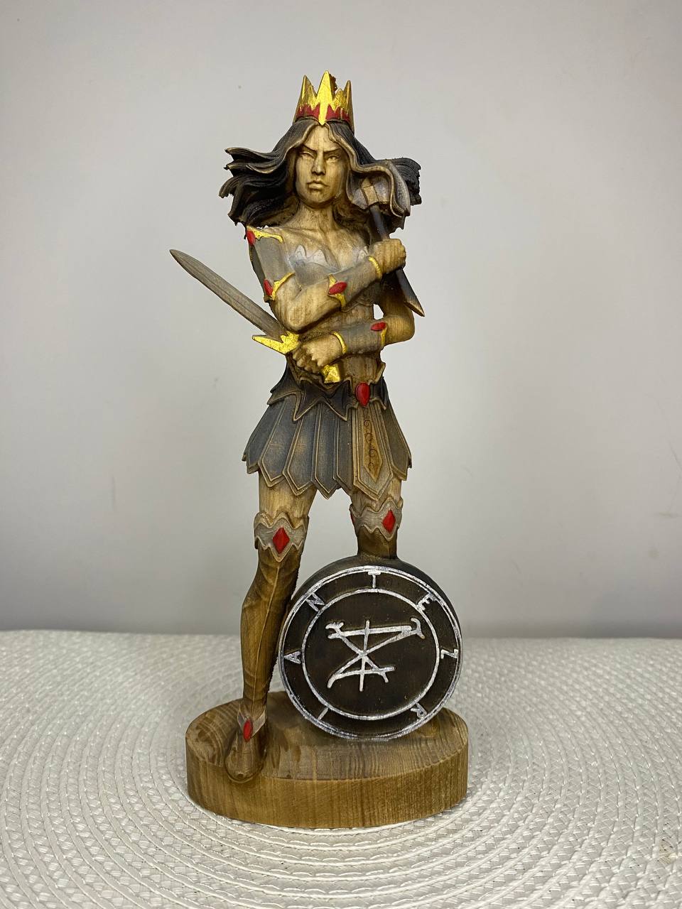 Hand carved wooden statue of Terzian, fantasy warrior queen with crown, sword, and shield bearing a mystical sigil, inspired by dark mythology and gothic fantasy decor.
