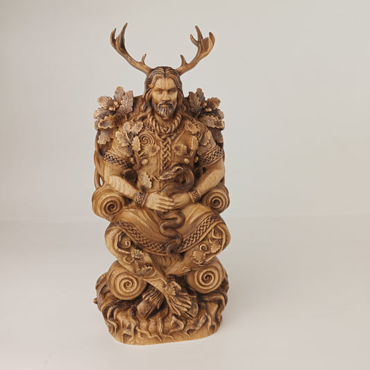 Intricately carved wooden statue of a horned forest deity seated on an ornate throne. The figure has large deer antlers, long hair, and a beard, holding a coiled serpent across his lap. Oak leaves, branches, and swirling Celtic-style carvings decorate the throne and base. The sculpture is photographed against a plain light background, highlighting the detailed wood grain and craftsmanship.