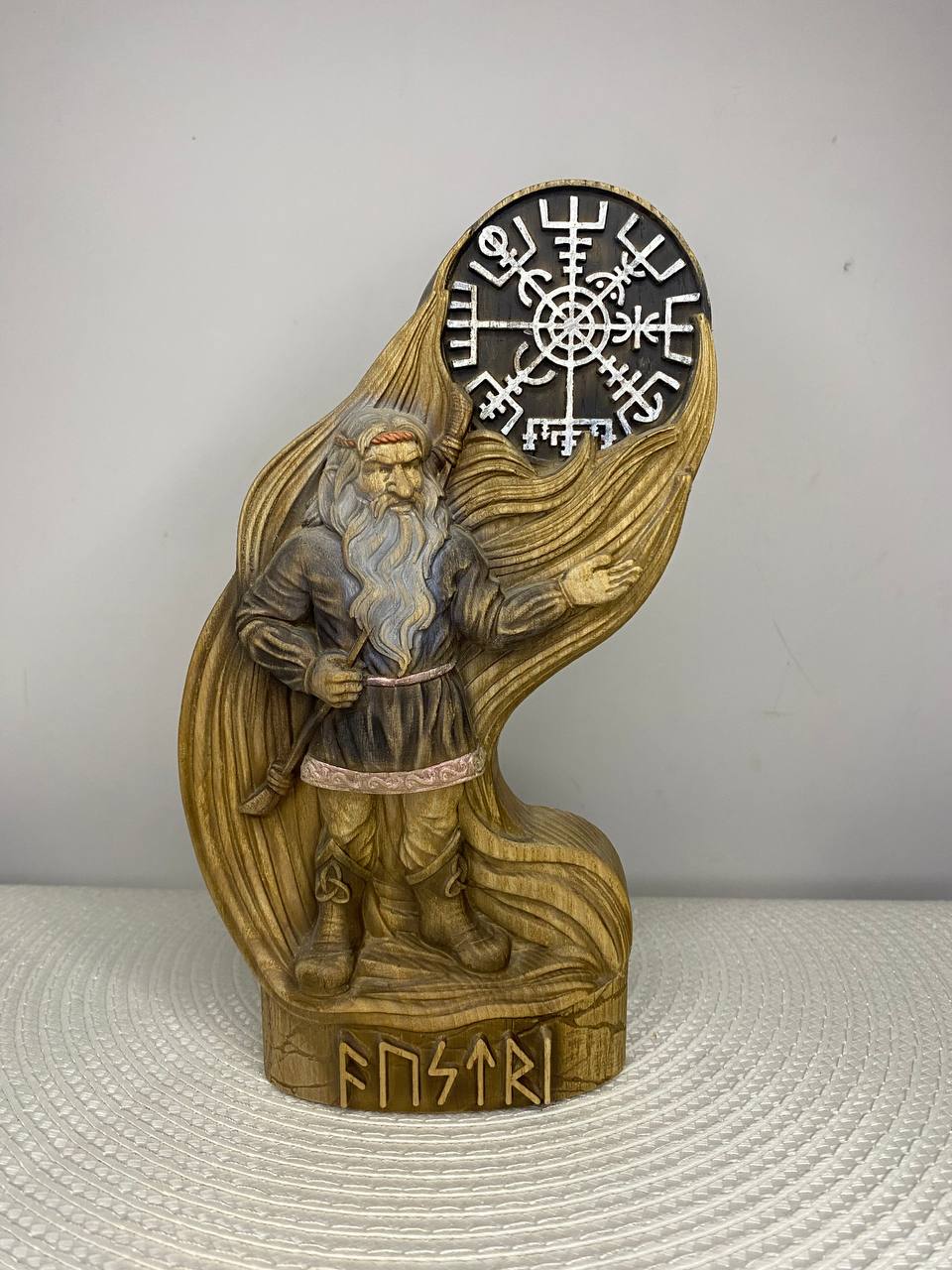 Austri Norse dwarf figurine, a hand-carved wooden Nordic gnome with a long braided beard, dark tunic, belt, and boots, standing beneath a large Norse symbol with runic carvings on the wooden base.