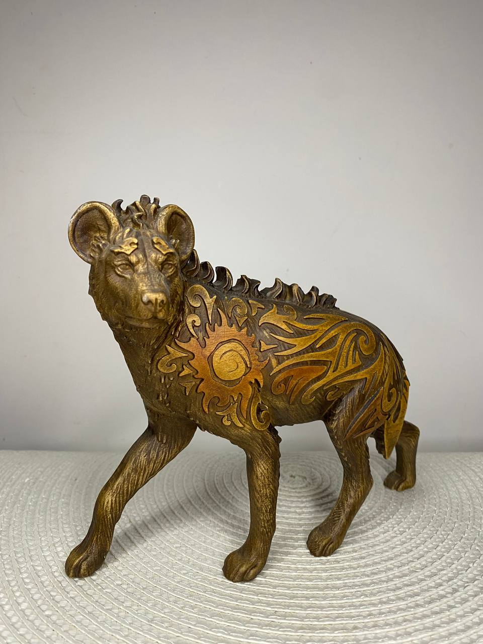 Handcrafted wooden hyena statue featuring intricate Celtic-inspired carvings, tribal sun motifs, and flowing ornamental patterns, hand-painted in black, gold, and bronze tones. Wildlife decor, African animal collectible, and unique wooden sculpture for home or altar display.