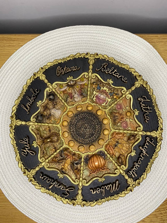 Top-down view of a hand-painted wooden Wheel of the Year plaque featuring the eight Wiccan sabbats—Yule, Imbolc, Ostara, Beltane, Litha, Lughnasadh, Mabon, and Samhain—surrounding a central solar motif, symbolizing seasonal cycles, nature-based spirituality, renewal, and pagan altar decor.
