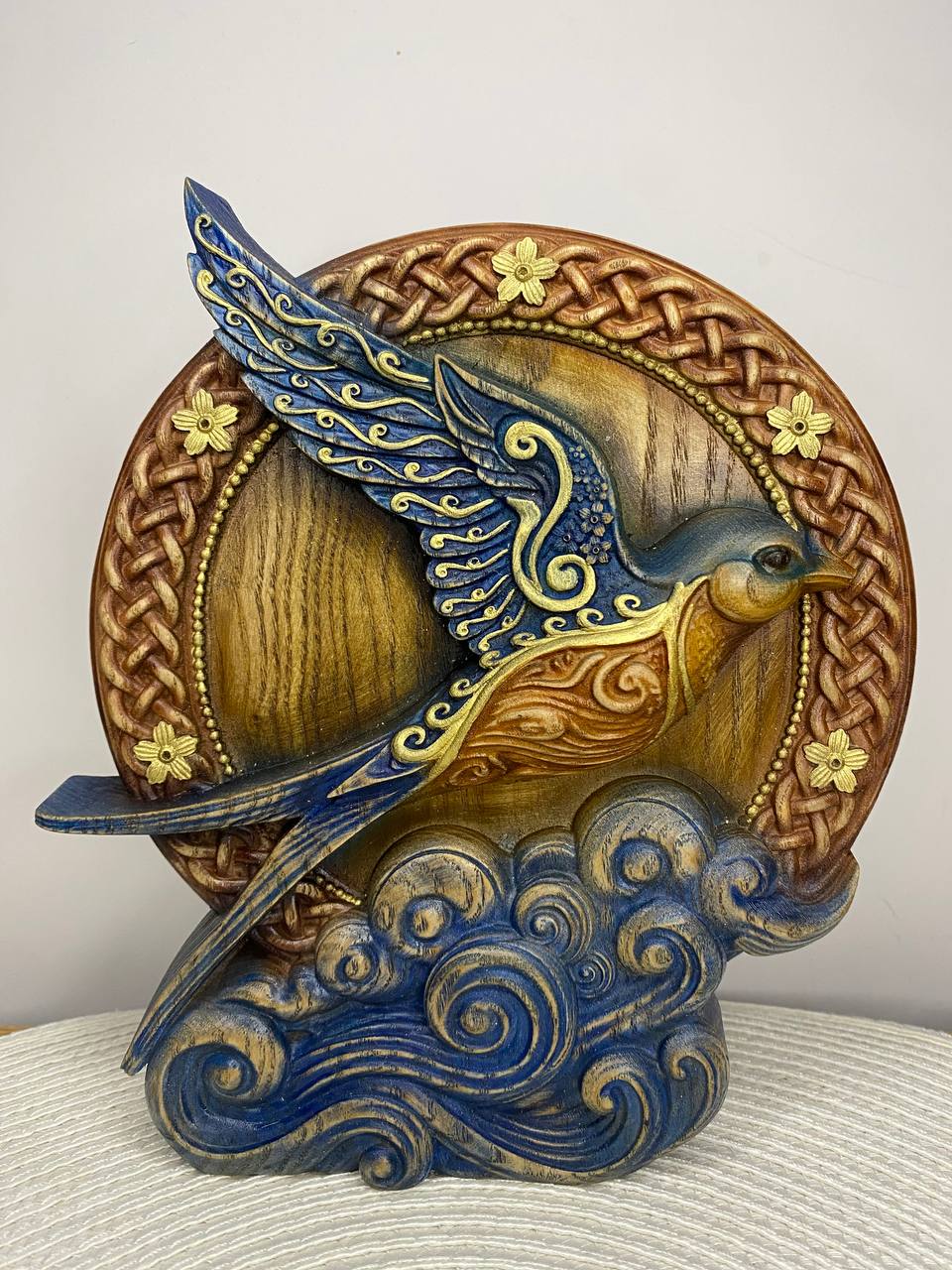 Handcrafted wooden Celtic blue bird statue featuring intricate knotwork, flowing waves, and a circular Celtic frame, hand-painted in rich blue, gold, and natural wood tones. Symbolic nature decor inspired by Celtic art, perfect for home, altar, or mythology collection.