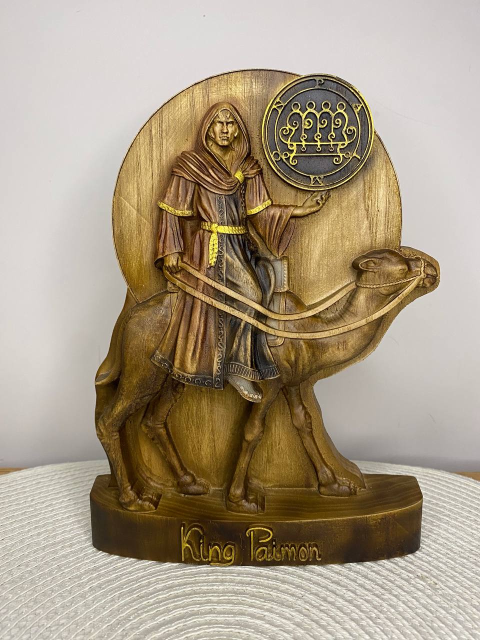 Handcrafted wooden King Paimon statue inspired by the Ars Goetia demon, depicting the crowned king riding a camel with his sigil displayed above, hand-painted in natural wood, gold, and bronze tones. Occult altar decor, demonology collectible, and Gothic fantasy sculpture.