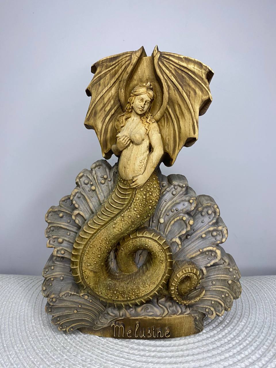 Handcrafted wooden Melusine statue inspired by European folklore, depicting the legendary winged serpent goddess with a coiled dragon tail rising from ocean waves, hand-painted in natural wood, gold, bronze, and gray tones. Fantasy mythology altar decor and collectible sculpture.